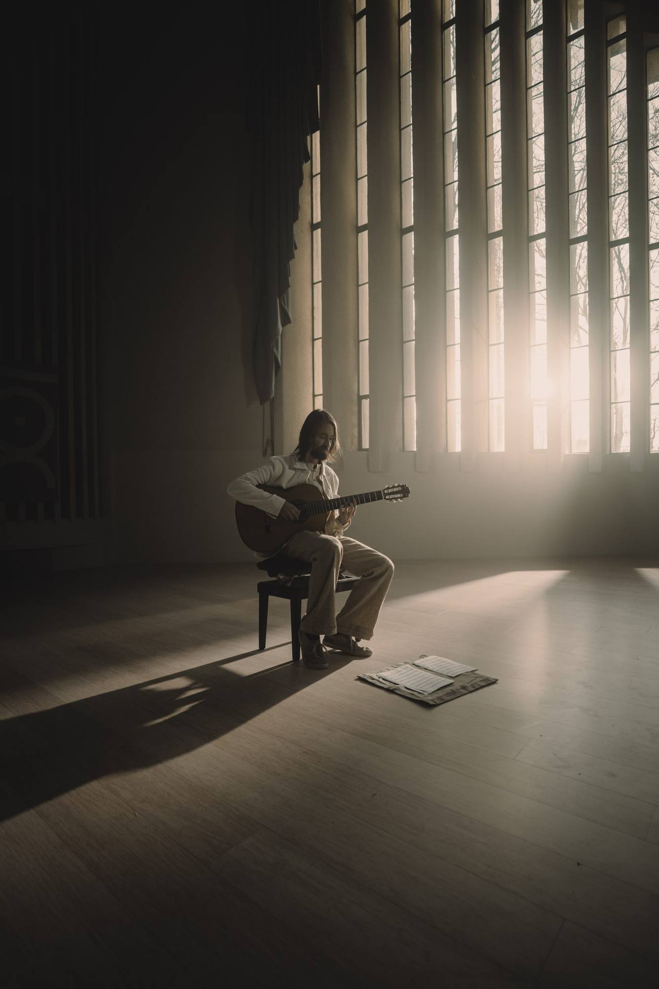 braem playing classical guitar in an empty hall, sunlight through tall windows